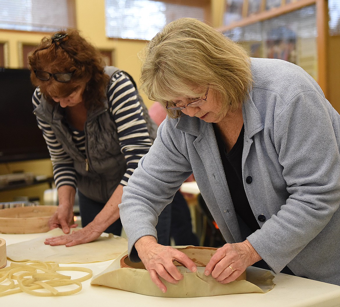 CHERYL COLLINS of Polson sizes her tanned hide around the edge of her cedar hoop. Sometimes the hide had to be stretched a little to cover the entire frame. In the background, Charlene Barber of Ronan stretches her hide. (Joe Sova photos/Lake County Leader)