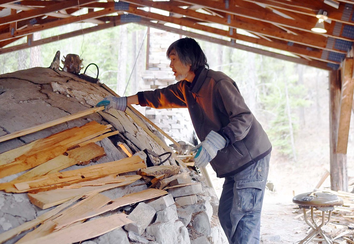 Potter Fuminori Deguchi loads wood into the side of the anagama kiln recently at Whitefish Pottery Studios on the Stillwater River. Several potters worked together for several days to keep wood-fired kiln going. (Heidi Desch/Whitefish Pilot)