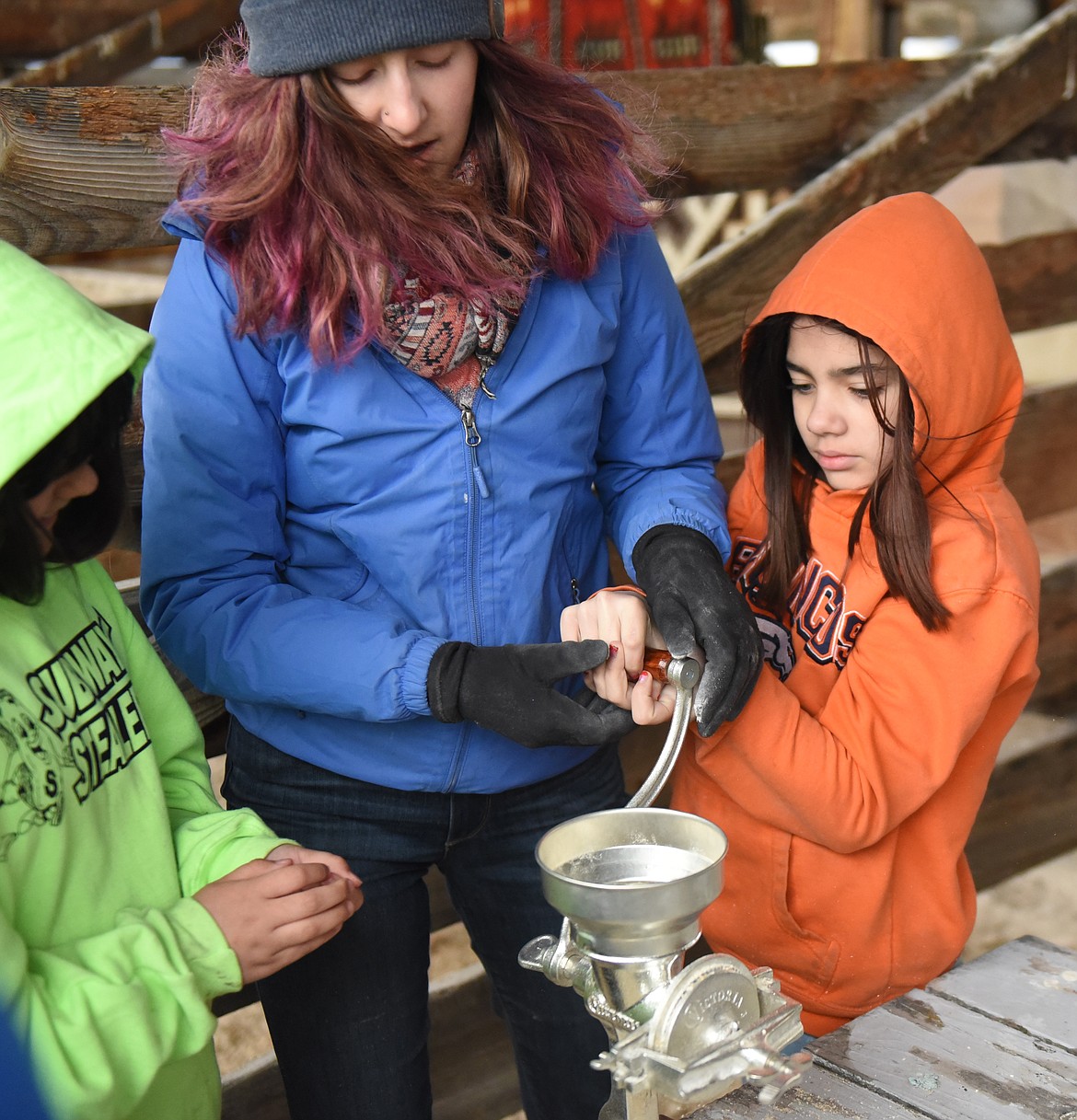 GRINDING GRAIN into flour is certainly hard work, as fourth-graders learned during Ag Day at the Polson Fairgrounds. Above, Aurorea Phillips gets help from Elena Shapiro of Food Core. Students also learned about soil erosion, raising livestock and other areas.