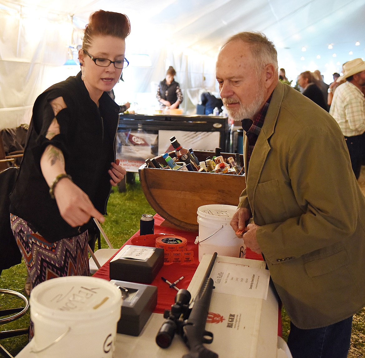 SHAWNA SIMONS points out the Ruger 270 rifle with Vortex scope that was offered in a raffle to Bob Martin during the Cowboy Ball. In the background is the Booze Barrel that was also raffled.