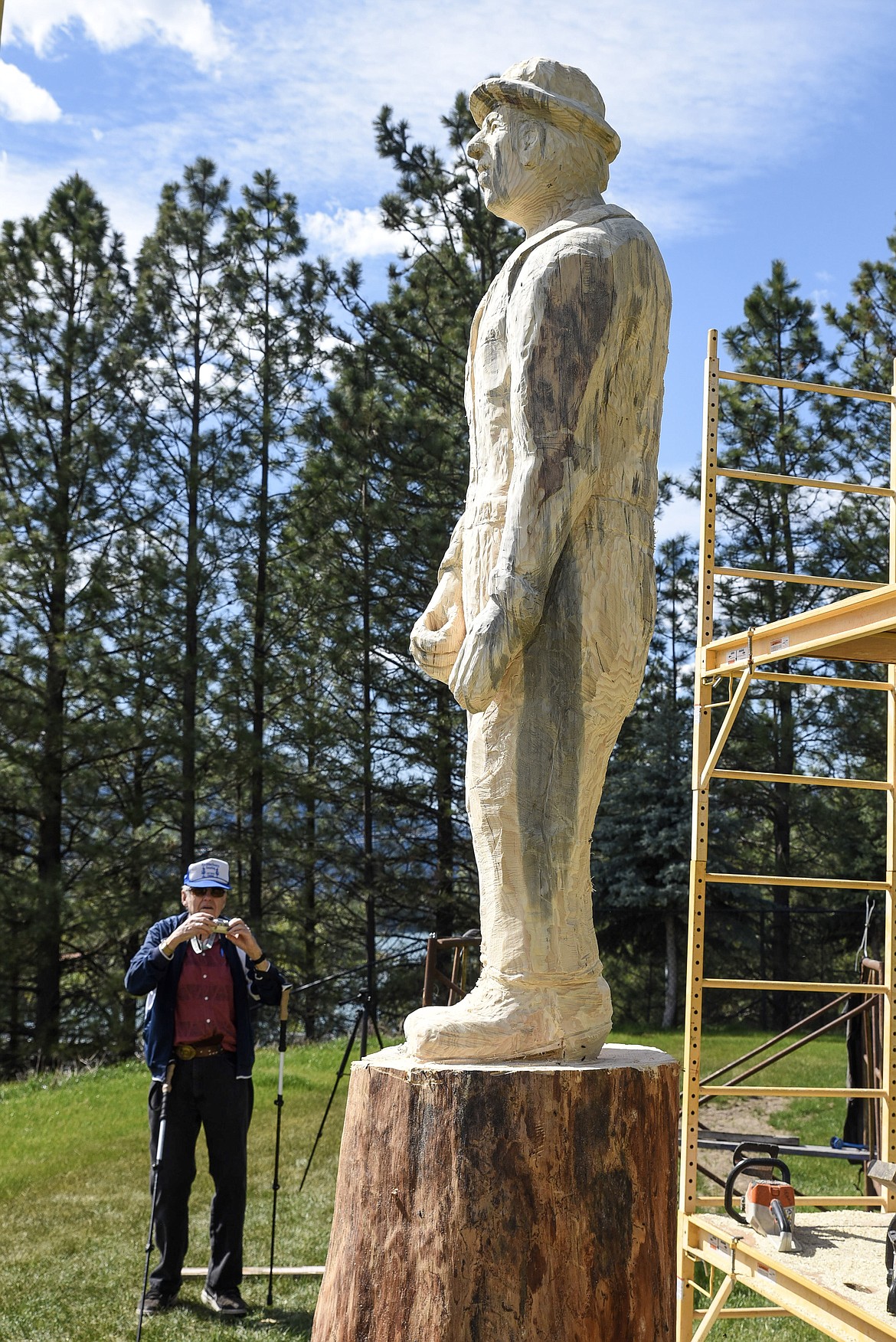 On a visit to check on progress, former forester Gene Yahvah takes a picture of the nearly-completed statue of a forester carved by local artist Ron Adamson. (Ben Kibbey/The Western News)