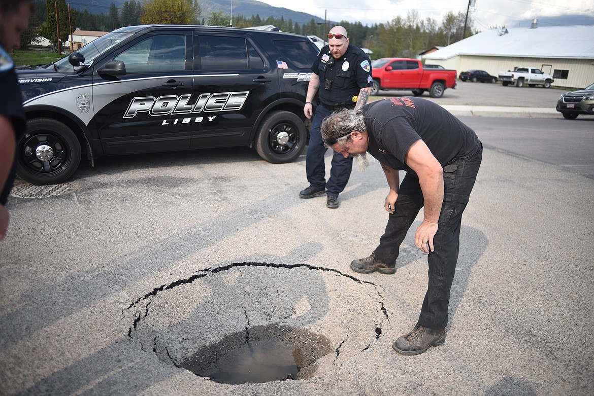 Mayor Brent Teske looks into a sinkhole on Montana Avenue while police officers block parts of the street, Tuesday in Libby. (Luke Hollister/The Western News)