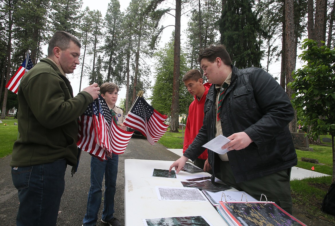 Benjamin Givens, right, instructs Scout Andrew Overland and Andrew's dad Dirk Overland where to place flags on veterans' graves Saturday morning in Forest Cemetery in Coeur d'Alene in observance of Memorial Day. Benjamin created an updated database of veterans laid to rest in Forest and Riverview cemeteries as part of his Eagle Scout project. Also pictured: Life Scout Will Meredith. (DEVIN WEEKS/Press)