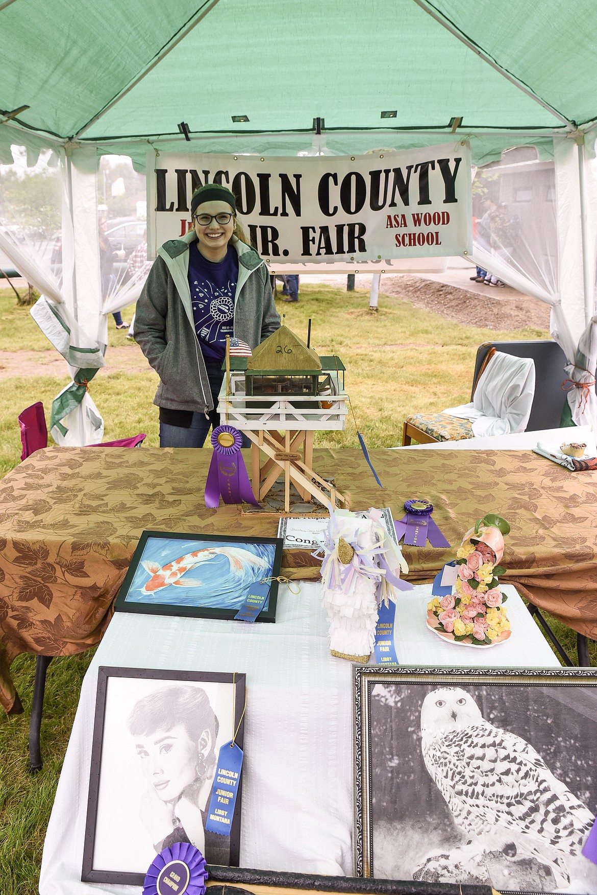Shelby Smith, promoting the Lincoln County Junior Fair, poses among some of the many entries she has submitted over the past six years, at the Kootenai Kiwanis Family Fun Day at Fireman&#146;s Park in Libby last Saturday. &#147;I want to spread the fun and joy that I experience doing the fair with other kids,&#148; Smith said. (Ben Kibbey/The Western News)