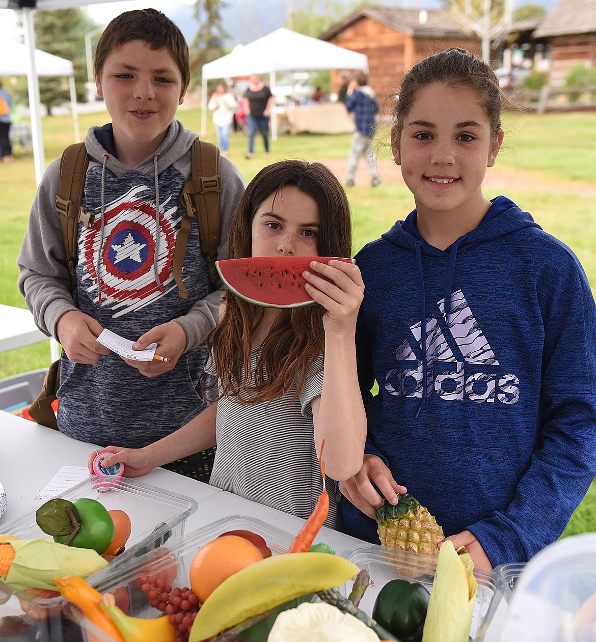 YOUNGSTERS LISTED their five favorite fruits at the POP Club booth in order to earn a token to spend at the Ronan Farmers Market. Completing their list, from left, are Parker Nolen, and Paisly and Novalii Corum.