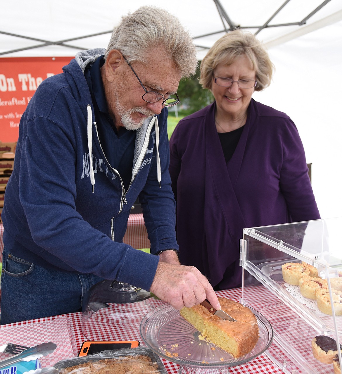 UNDER THE watchful eye of his wife, Mary, Rusty Carl carefully carves a delicious lemon cornmeal cake at the Farmers Market booth. Their business is Home on the Range Pies, now in their 10th year, out of Ronan.