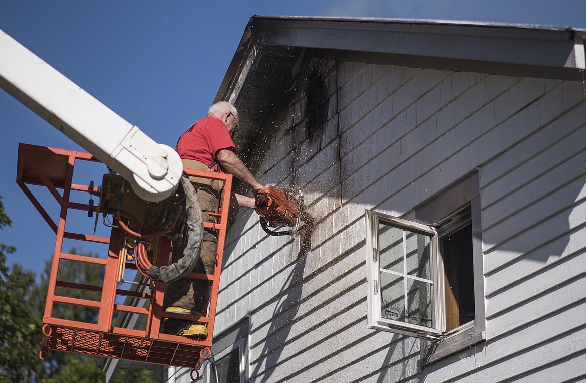 Troy Volunteer Fire Department Fire Marshal Gene Rogers cuts a hole in order to spray the attic of a house on fire in Troy, early Tuesday morning along Riverside Avenue. (Luke Hollister/The Western News)