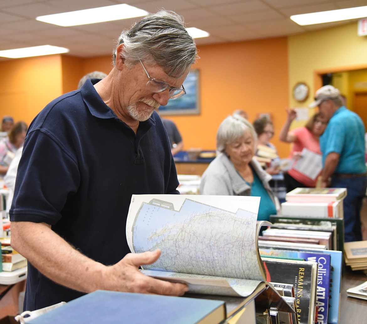 DENNIS WINTER of Ronan is a 31-year U.S. Navy veteran who is still intrigued by books, such as the atlas he is holding during the Used Book Sale May 31 and June 1 in Polson. The sale included movies and audto books.