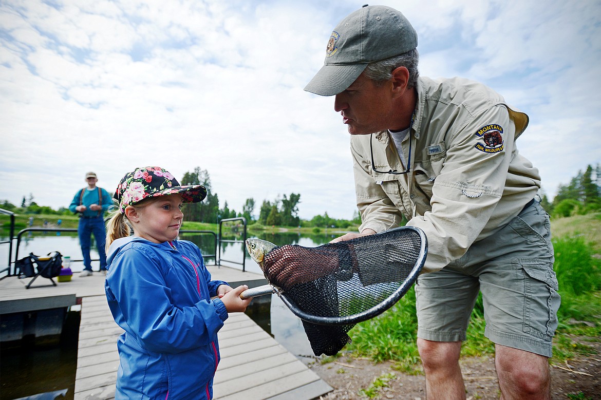 Channa Melnick, 8, of Kalispell, reacts as she comes face-to-face with a rainbow trout she caught during the Robin Street Memorial Family Fishing Day hosted by Montana Fish, Wildlife &amp; Parks at Pine Grove Pond in Kalispell on Saturday. Holding the catch is Dave Hagengruber, angler education coordinator with Montana FWP. (Casey Kreider/Daily Inter Lake)