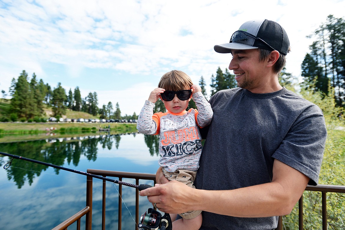 Silas Sekera, 2, of Kalispell, tries on a pair of sunglasses, one of many items handed out by Montana Fish, Wildlife &amp; Parks, as he fishes with his father Nathan during the Robin Street Memorial Family Fishing Day at Pine Grove Pond in Kalispell on Saturday. (Casey Kreider/Daily Inter Lake)