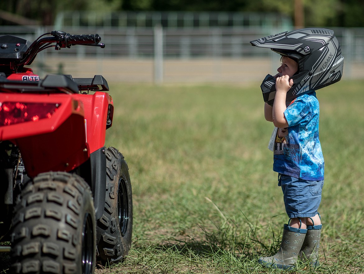 Caleb Peterson, wearing his new helmet, takes a long look at a quad on display during a 4-wheeler training workshop for children at J. Neils Memorial Park, Tuesday. (Luke Hollister/The Western News)