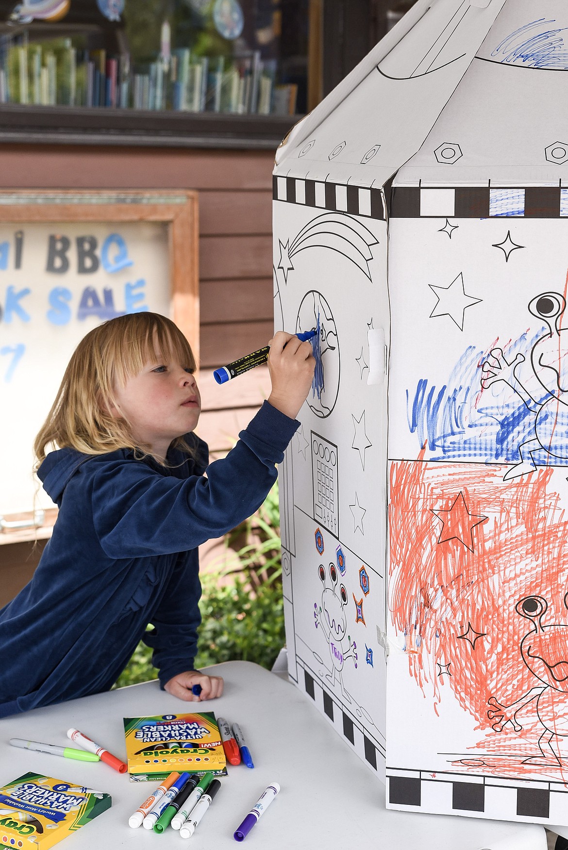 Isabella Salusso, who was with her parents visiting family from the Yaak, colors on the large rocket at the Troy Library on Friday, June 7, during the annual Barbecue and Book Sale. (Ben Kibbey/The Western News)