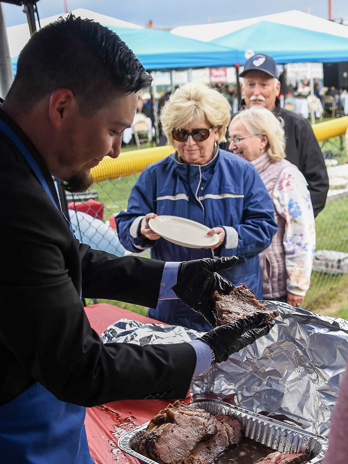 Libby Loggers assistant Coach Joe Flores takes a look at one of the slices of prime rib he was serving during Dinner on the Diamond at Lee Gehring Memorial Field Friday. (Ben Kibbey/The Western News)