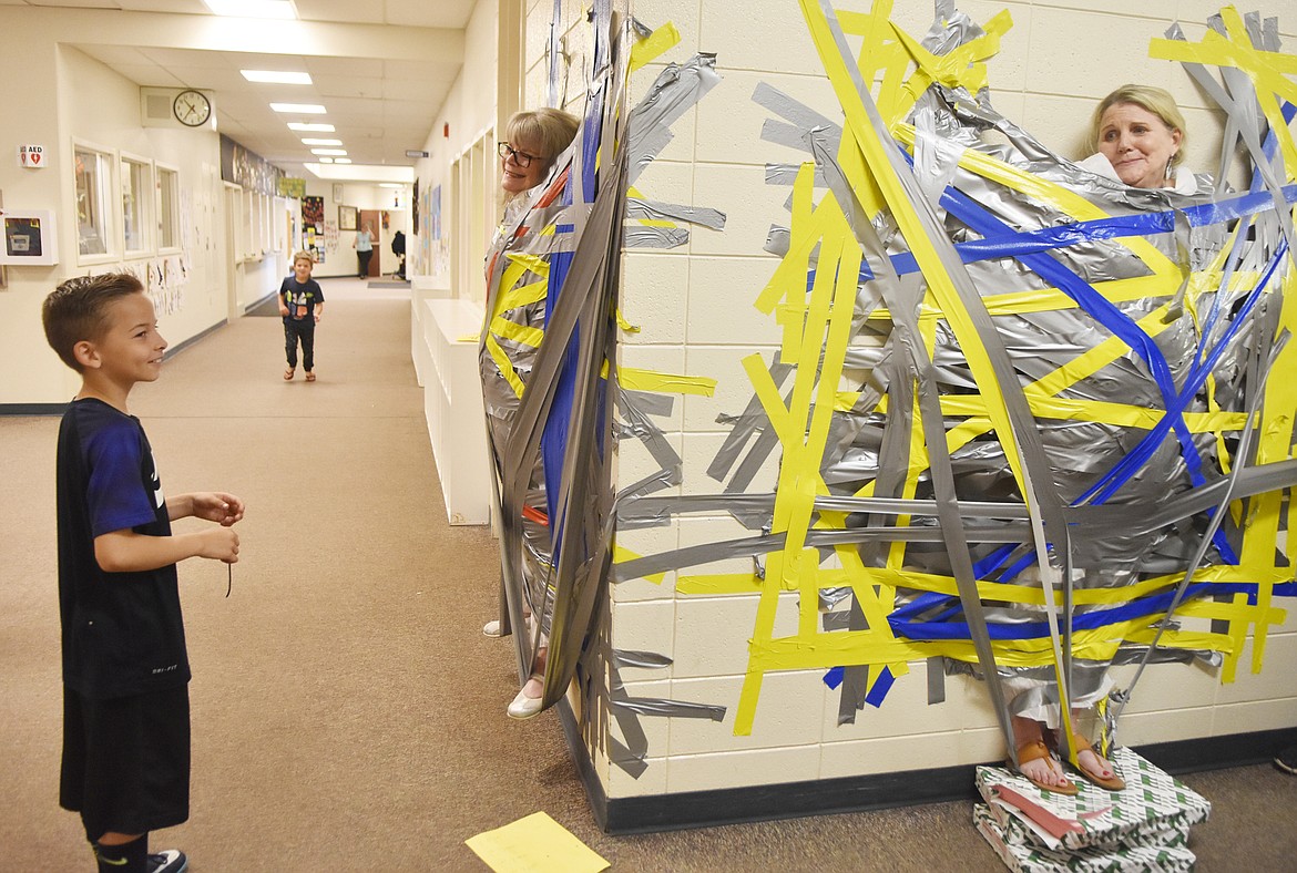 Muldown Elementary student Coy Moss talks with Principal Linda Whitright, left, and Counselor Kelly Talsma while both are duct-taped to the walls of the school Wednesday morning. Students got to tape two counselors and two administrators to the wall in celebration of their efforts during the Muldown Fun Run. (Heidi Desch/Whitefish Pilot)