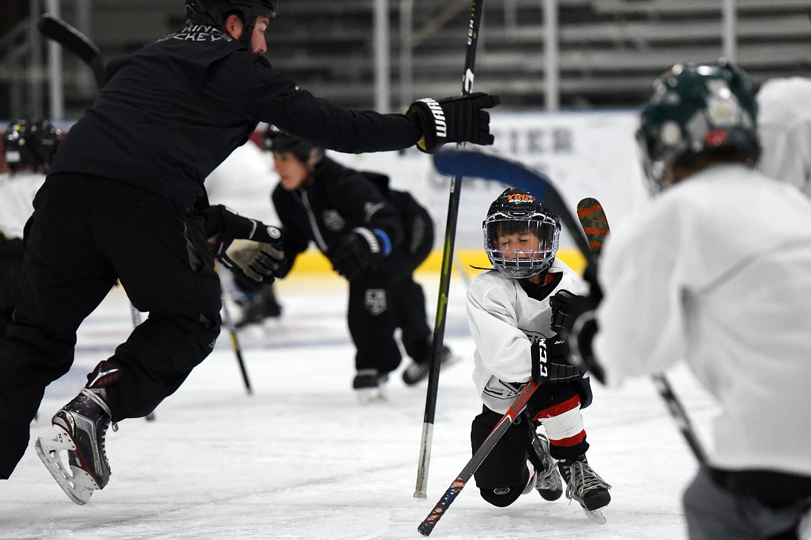 Vinni Ferruzzi, 6, of Missoula, grabs his hockey stick before it could fall to the ice during a drill with Courtney Ports, left, manager of hockey development with the Los Angeles Kings, at the L.A. Kings Summer Camp-Whitefish at Stumptown Ice Den in Whitefish on Thursday. During the drill, campers were instructed to stand their sticks up and, once a whistle was blown, grab their fellow campers' stick before it could fall to the ice. (Casey Kreider/Daily Inter Lake)