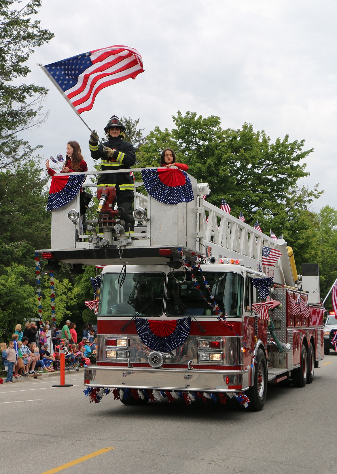 (Photo by CAROLINE LOBSINGER)A Selkirk Fire firefighters waves the American flag during the Sandpoint Lions' Fourth of July Grand Parade on Thursday.