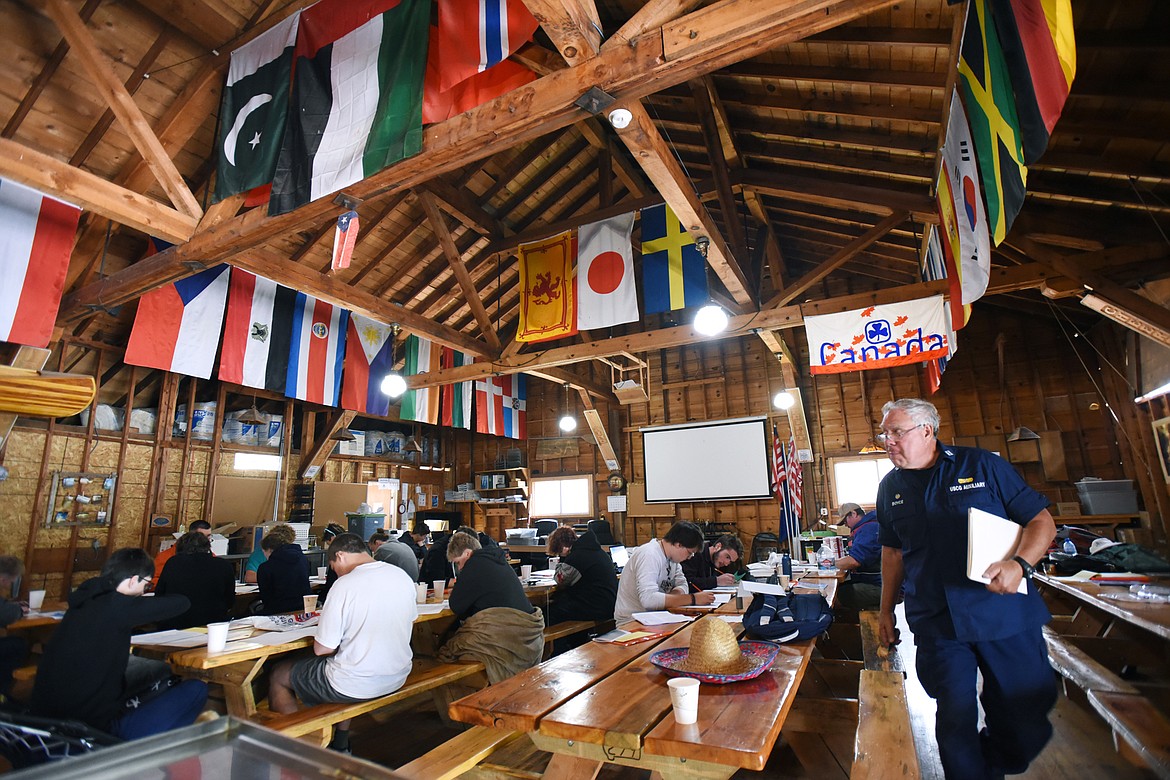 Kyle Boyce, U.S. Coast Guard Auxiliary Flotilla Commander, walks past a group of Boy Scouts and Venture Scouts taking an exam inside the Ragsdale Lodge on Camp Melita Island on Flathead Lake near Big Arm on Tuesday, June 25. The lodge was built in 1922 and dedicated to Master Sgt. Eugene H. Ragsdale with the U.S. Air Force. (Casey Kreider/Daily Inter Lake)