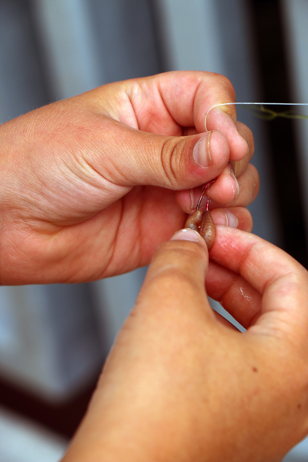 (Photo by CAROLINE LOBSINGER)Max Solis fits a worm onto a hook as he prepares to go fishing in Sand Creek on Thursday.