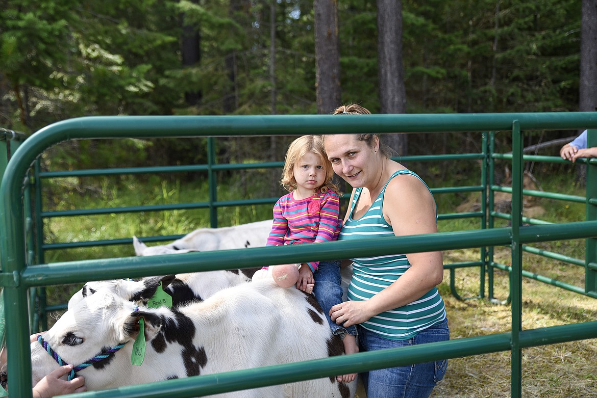 Annika Meyer sits on a cow that is a 4-H project for Brooklynn and Zeeannah Reid (not pictured) while her aunt, Katie Reid, holds onto her, at the Three Lakes Roundup, put on by Three Lakes Community Bible Church, Saturday. (Ben Kibbey/The Western News)