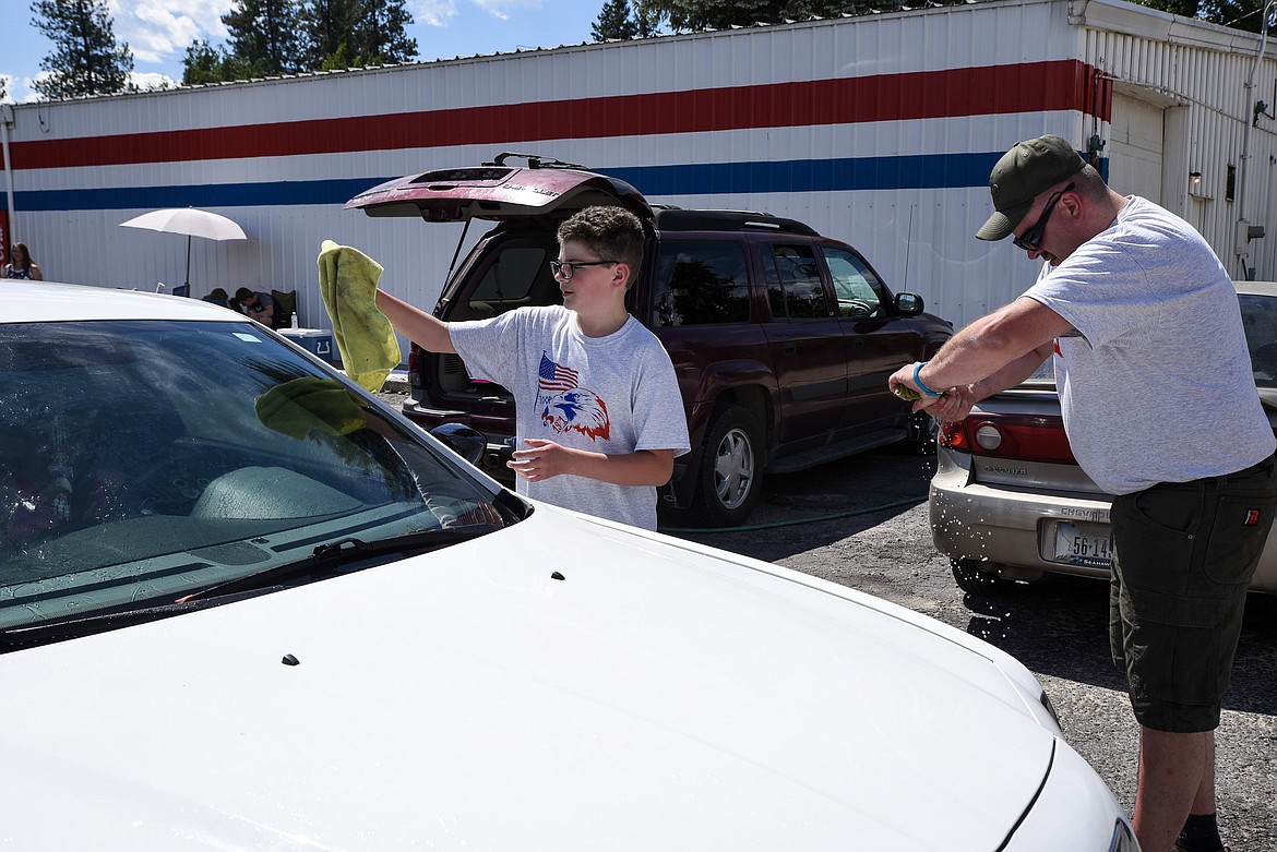 Tenderfoot Warren Paulsen dries while his dad, Assistant Scout Master Kim Paulsen, wrings out his cloth, at a car wash to raise money for Boy Scout Troop 1971 to make a a trip to Camp Meriweather, Oregon, at Carquest Auto Parts Saturday. (Ben Kibbey/The Western News)