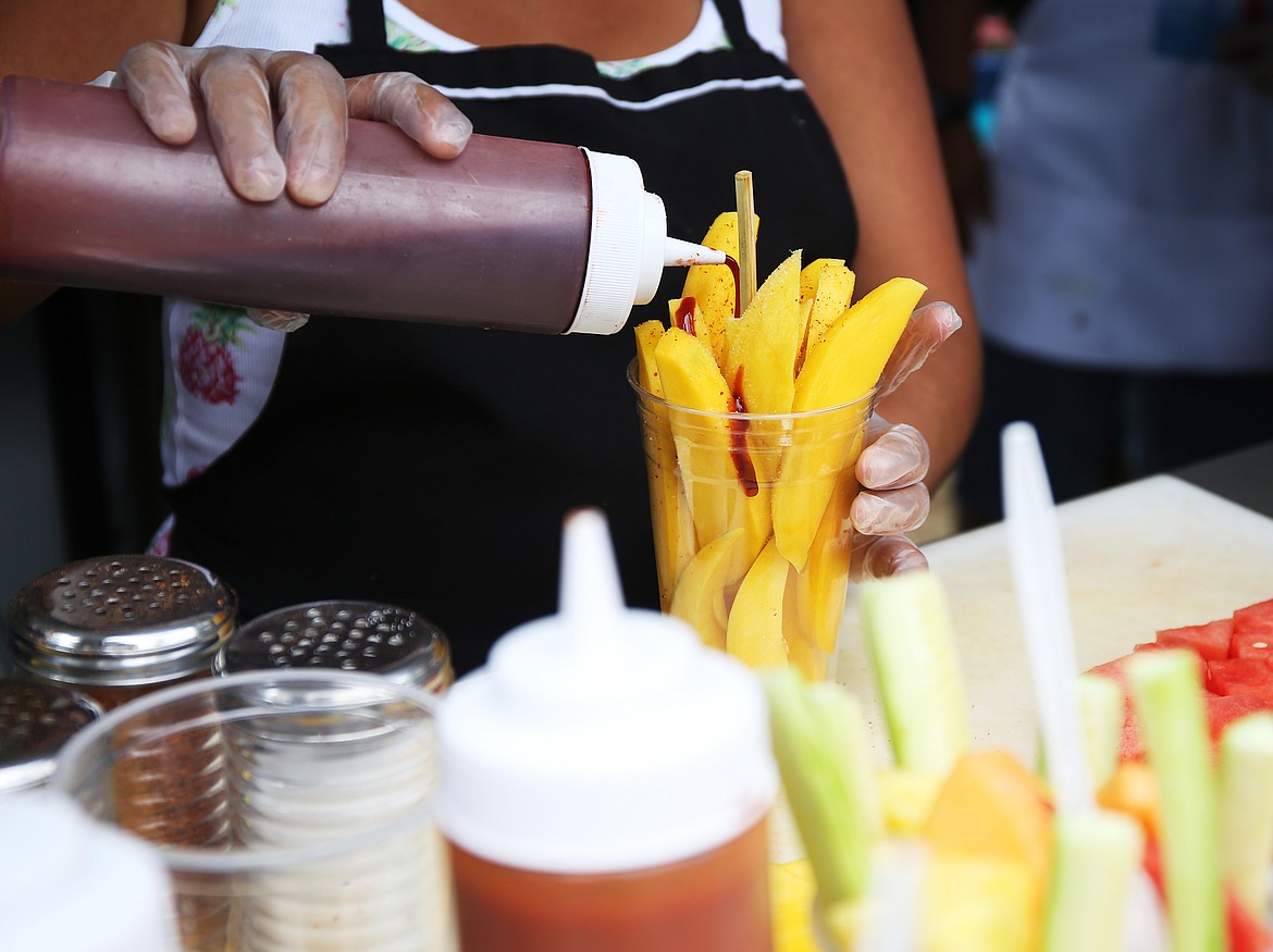 Mary Pena with Raspado Del Sur pours Camoy flavor sauce on mangos during Taste of Coeur d'Alene 2018. (LOREN BENOIT/Press File)