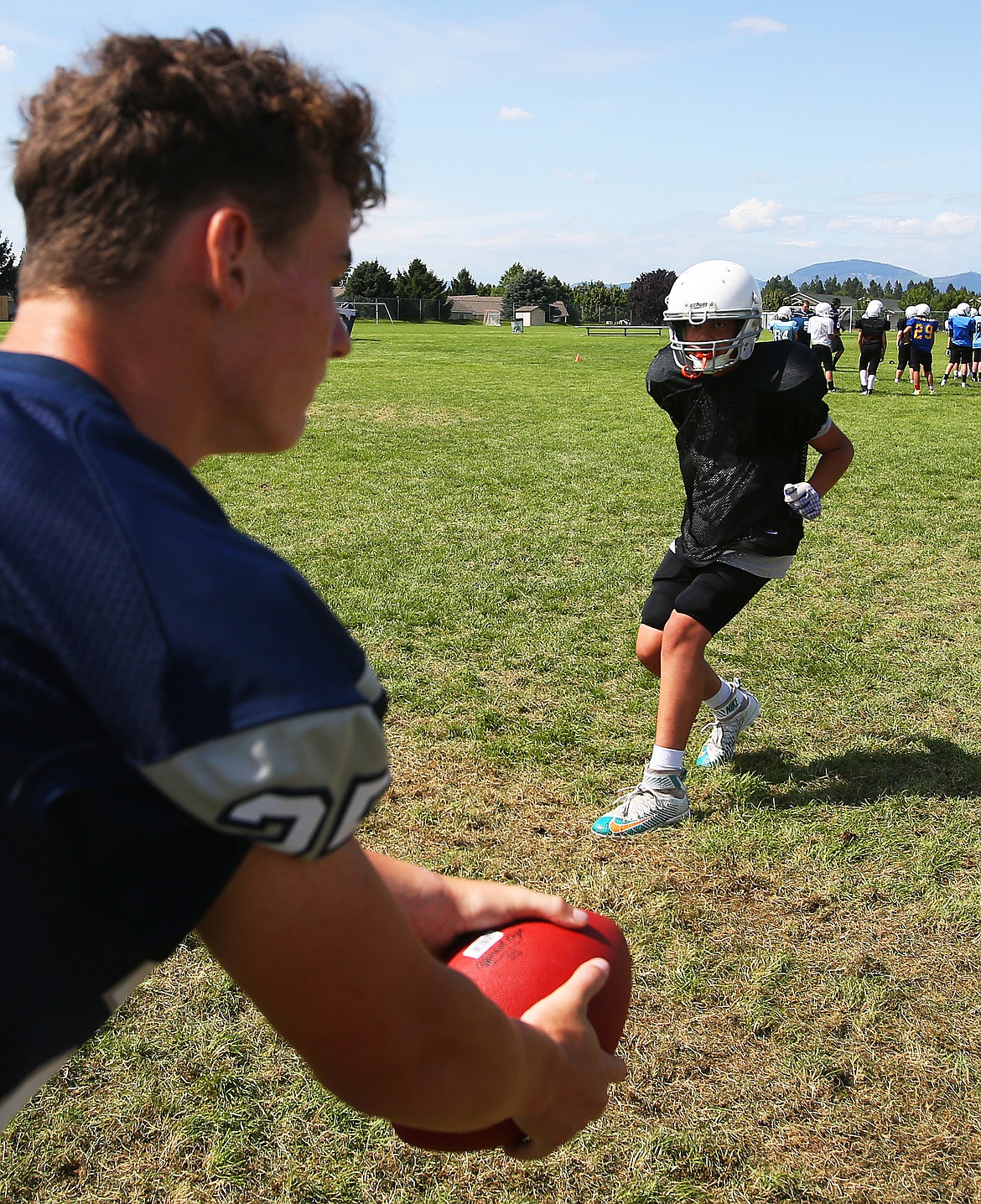 Lake City High School junior Porter Howard, left, hikes the ball as Joseph Petree, a Woodland Middle School eighth-grader, backpedals to cover a route during a drill Friday at Junior Tackle camp.