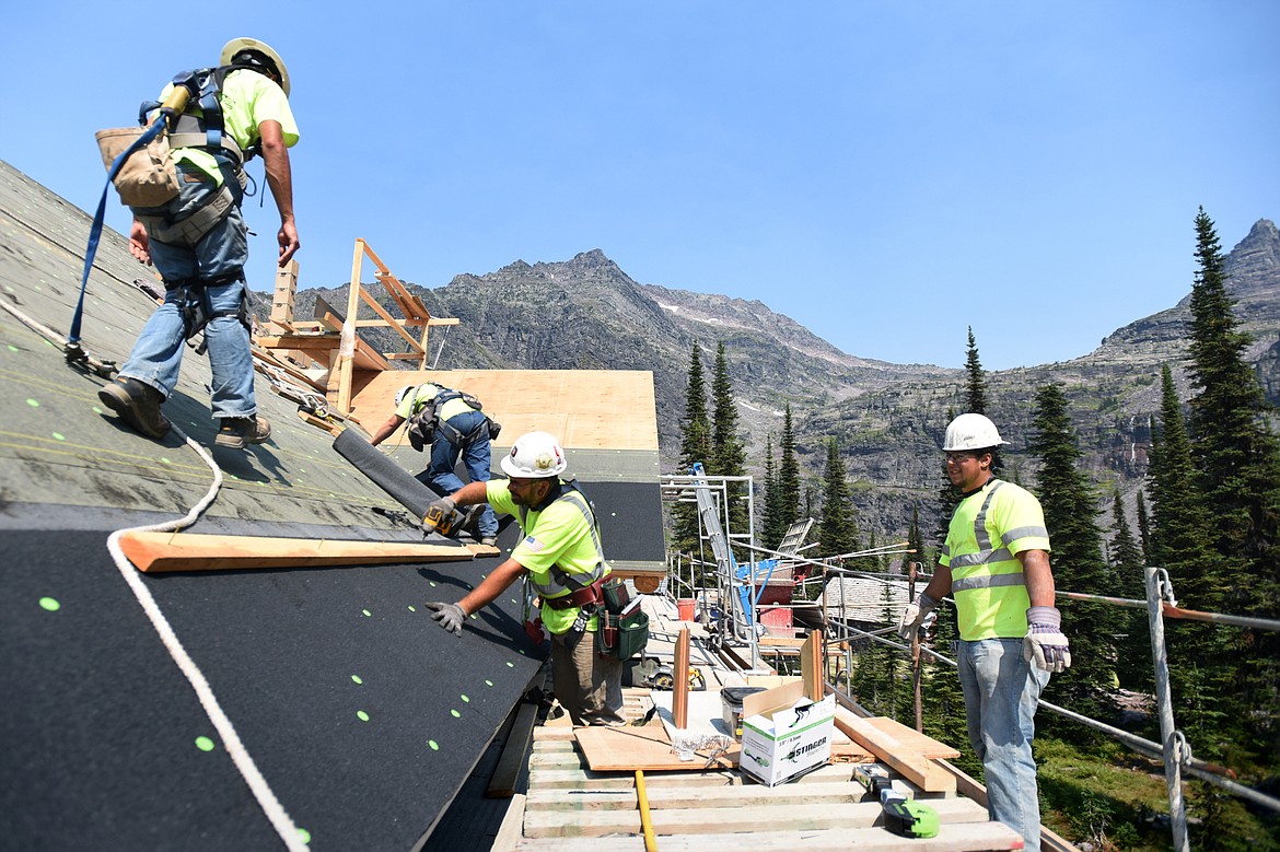 From left, Dick Anderson Construction employees Jack Mueller, Jason Burks and Jason Williams install a roofing membrane as Jeremy Bercier, with Anderson Masonry, makes his way along the catwalk of the Sperry Chalet in Glacier National Park on Aug. 8. (Casey Kreider photos/Daily Inter Lake)