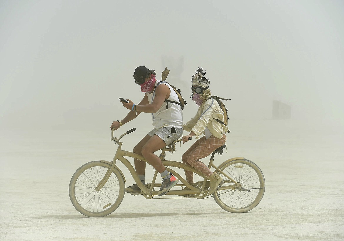 In this Aug. 30, 2018, photo, a burner checks his phone as he rides a unicycle through a dust dust storm at Burning Man, in Gerlach, Nev. Breakfast, lunch and dinner at Burning Man is served with a side of playa dust that covers cars and clothing and finds its way into places where the sun doesn&#146;t shine. (Andy Barron/The Reno Gazette-Journal via AP)