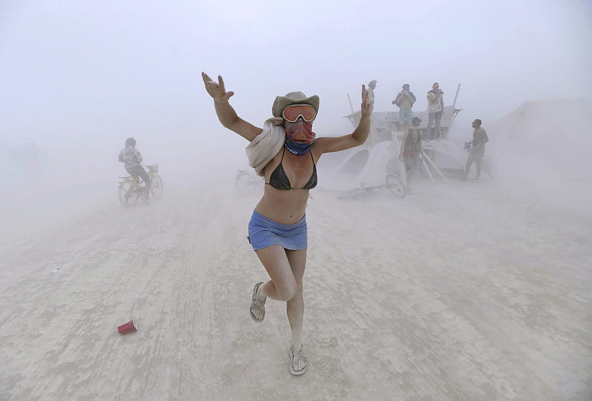 In this Tuesday, Aug. 29, 2017, photo, Rebeccah Sheftall dances during a dust storm at Burning Man, in Gerlach, Nev. Breakfast, lunch and dinner at Burning Man is served with a side of playa dust that covers cars and clothing and finds its way into places where the sun doesn&#146;t shine. (Andy Barron/The Reno Gazette-Journal via AP)