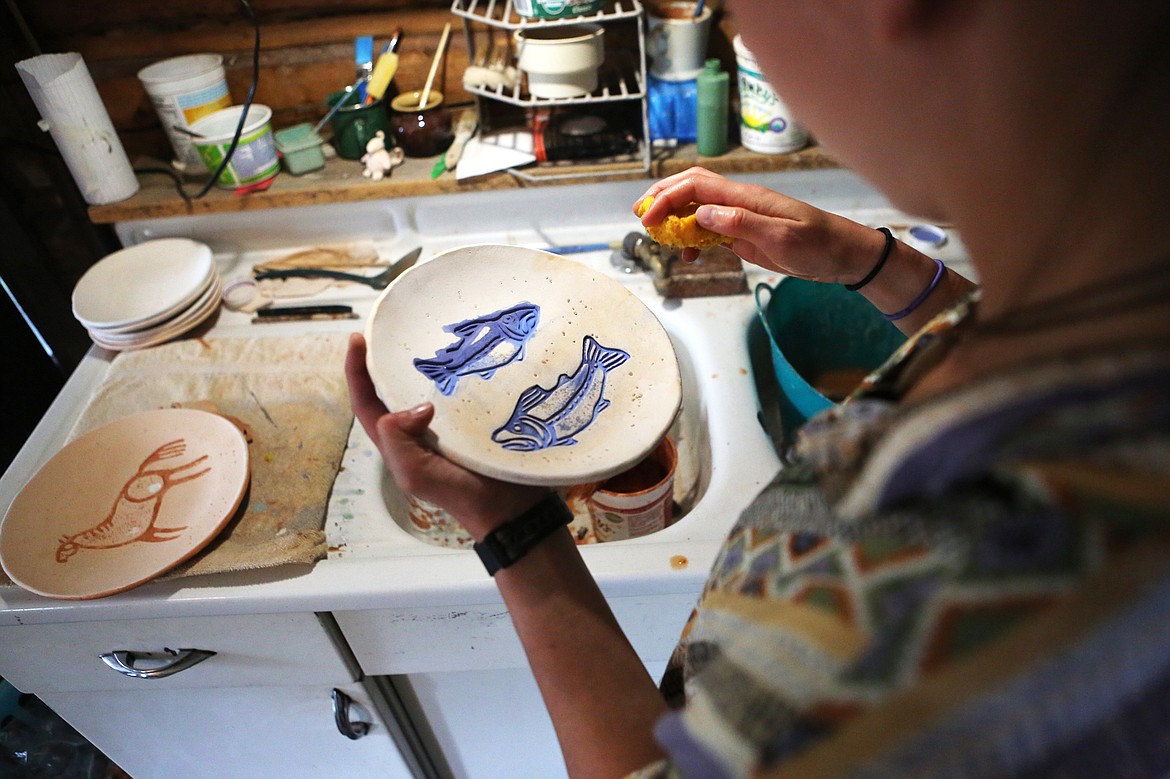 Potter Casey Fuson wipes excess glaze from a plate inside her studio, a 102-year-old cabin in rural Trego. (Mackenzie Reiss/Daily Inter Lake)