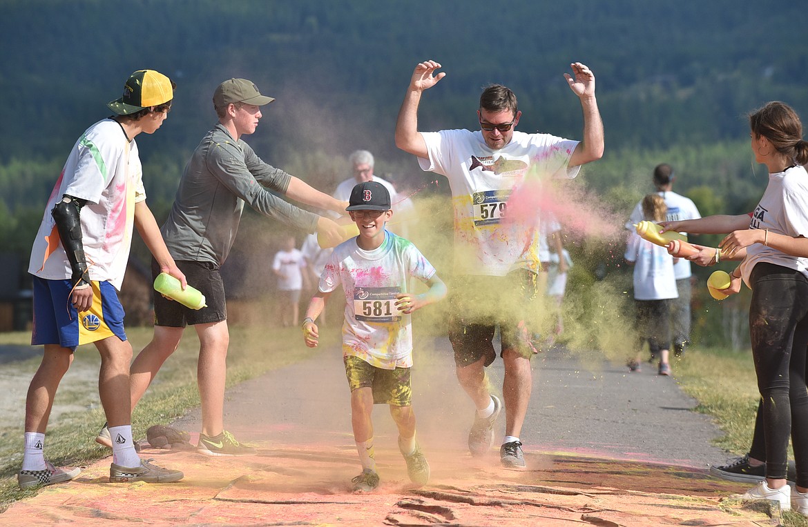 Luke Sol Bonds, 10, followed by Tim Bonds run through the green and yellow station Saturday morning during the Great Fish Community Challenge Color Run through Whitefish. (Heidi Desch/Whitefish Pilot)