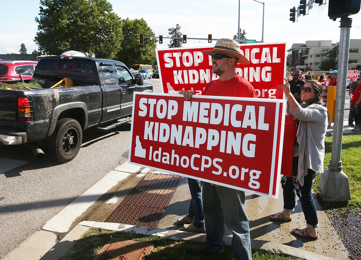 Guy McAninch and his wife, Tamara, of Post Falls, hold signs at the intersection of Ironwood Drive and U.S. 95 Wednesday afternoon. The couple and around 40 others stood next to Kootenai Health to voice their stance on how Kootenai Health and CPS handle childcare treatment. (LOREN BENOIT/Press)