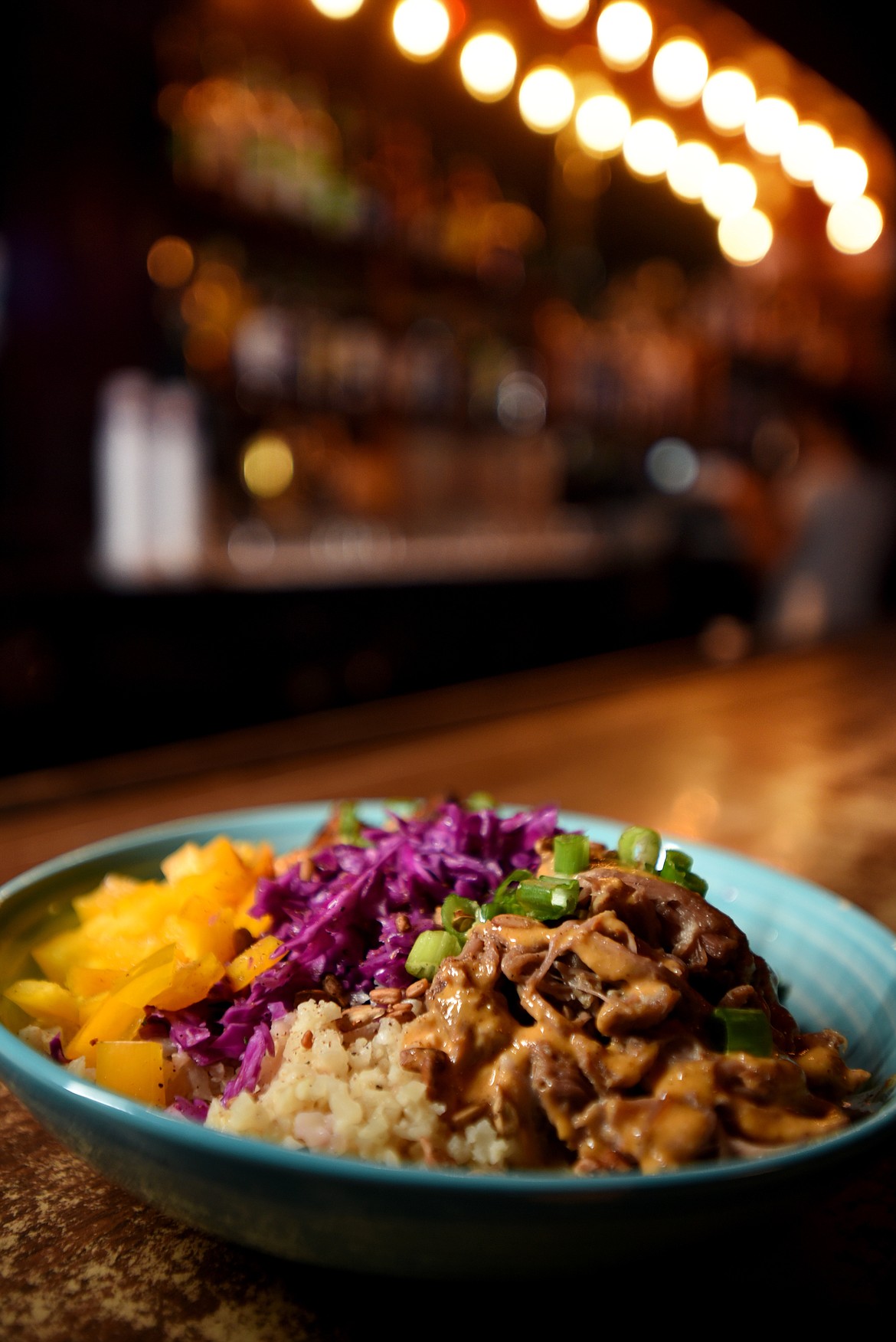 The Rebel Rice Bowl features crispy Hoisin tofu and Kalua pulled pork with cauliflower rice, organic kale salad, purple cabbage, bean sprouts, raw bell peppers, lightly steamed Sriracha butter carrots, and toasted sunflower seeds, topped with yellow curry coconut sauce.