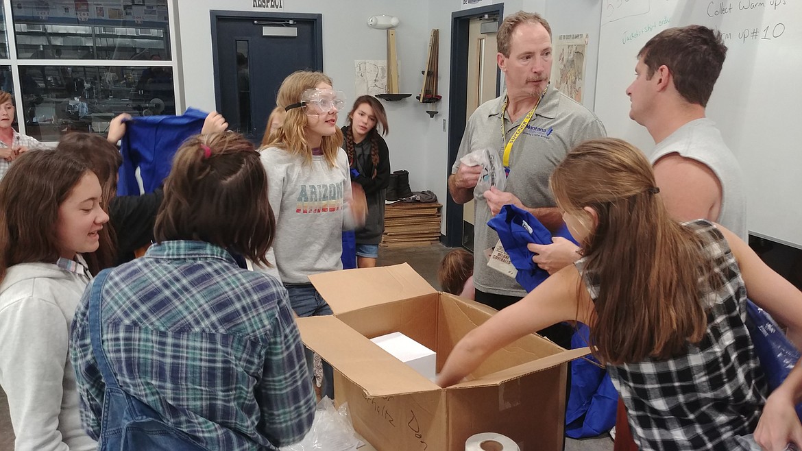 MARK LEAFMAN, Montana State Fund consultant and Superior shop class teacher Jeff Schultz hand out safety coveralls to students in Schultz's 7th grade shop class. (Chuck Bandel/Mineral Independent)