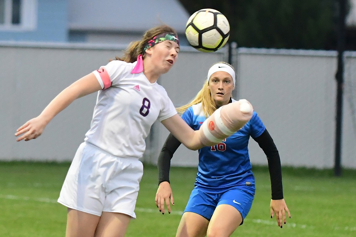 Lady Pirate Megan Rost (8) heads the ball during play at Columbia Falls. Rost ordinarily plays goalkeeper, the only player in soccer allowed to use her hands. Looking on is WildKat (16) Flora Jarvis.The cast Rost is wearing is to protect a broken finger she sustained while attending a gridiron football game when an overzealous fan ripped a flag out of her grasp, taking her finger along with it. (Jeremy Weber/Hungry Horse News)