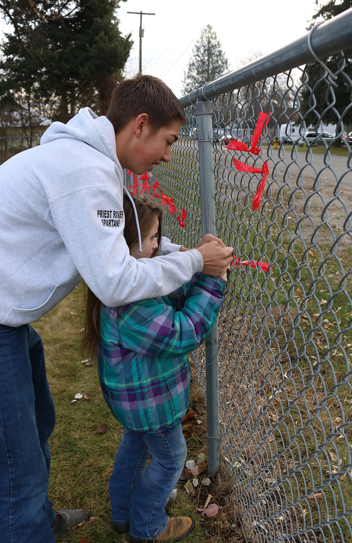 (Photo by MARY MALONE)
Priest River Lamanna High School sophomore Bowen Fegert helps an Idaho Hill Elementary student tie a red ribbon to the fence in honor of National Red Ribbon Week on Oct. 28.