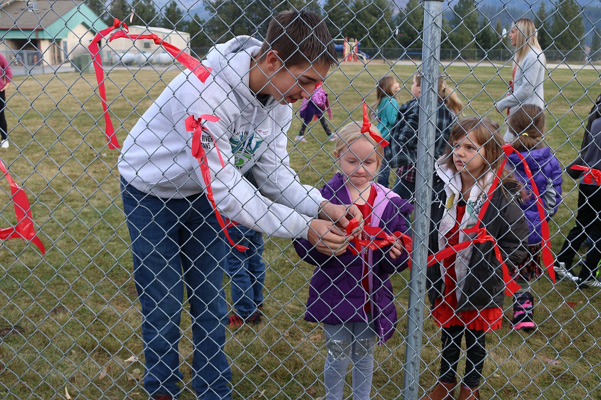 (Photo by MARY MALONE)
Priest River Lamanna High School sophomore Bowen Fegert helps an Idaho Hill Elementary student tie a red ribbon to the fence in honor of National Red Ribbon Week.