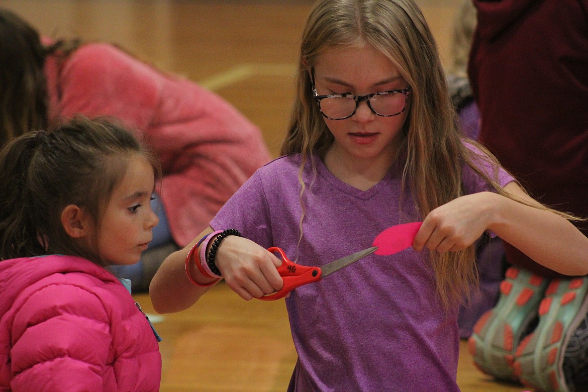 LEXI FRANCK (with the scissors) helps Sydney Lofthus cut out her footprint last Wednesday. (John Dowd/Clark Fork Valley Press)