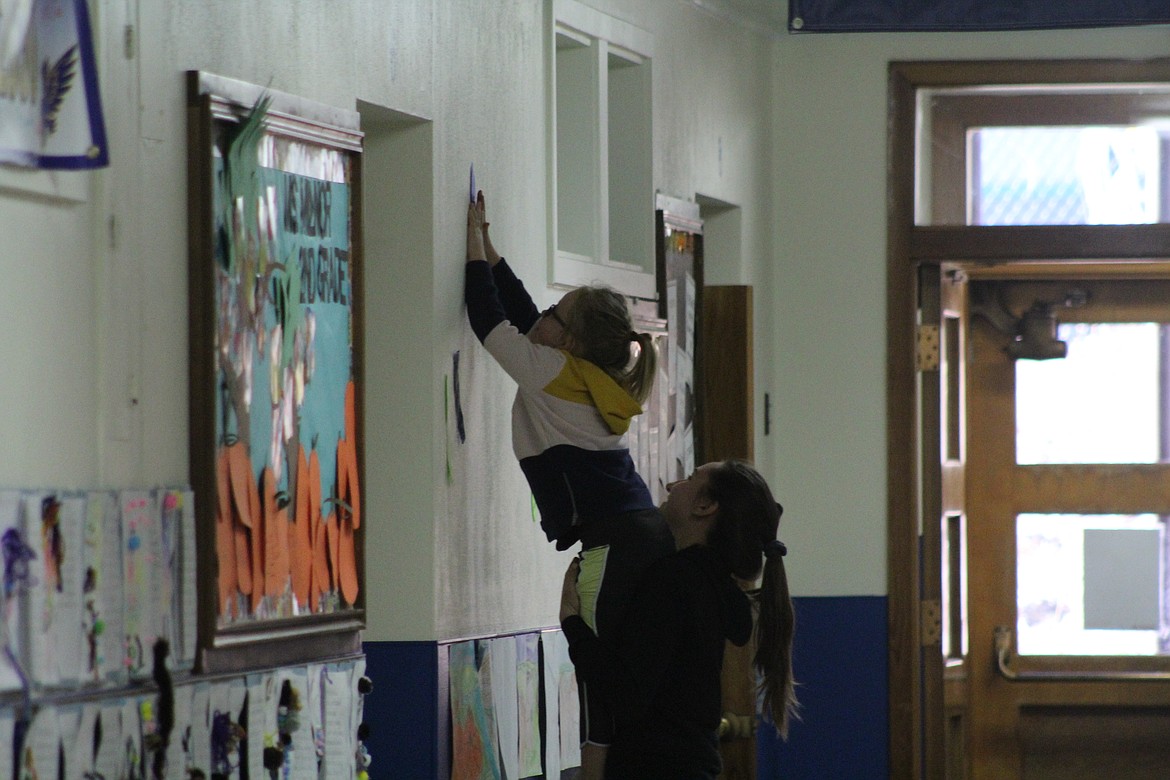 KAILEY BROWN helps a younger student place her footprint high on the wall. (John Dowd/Clark Fork Valley Press)