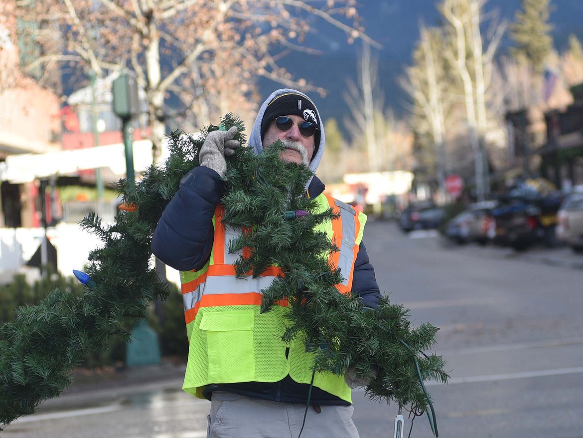 Dan Fischer holds one end of garland as volunteers hang winter decorations downtown Sunday morning. (Heidi Desch/Whitefish Pilot)