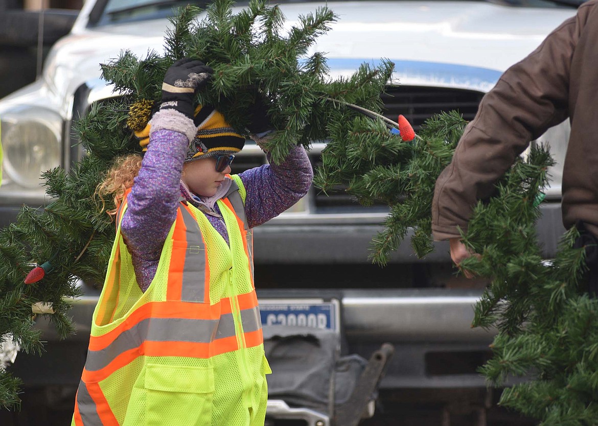 Trinity Workman holds a section of garland Sunday morning downtown. (Heidi Desch/Whitefish Pilot)