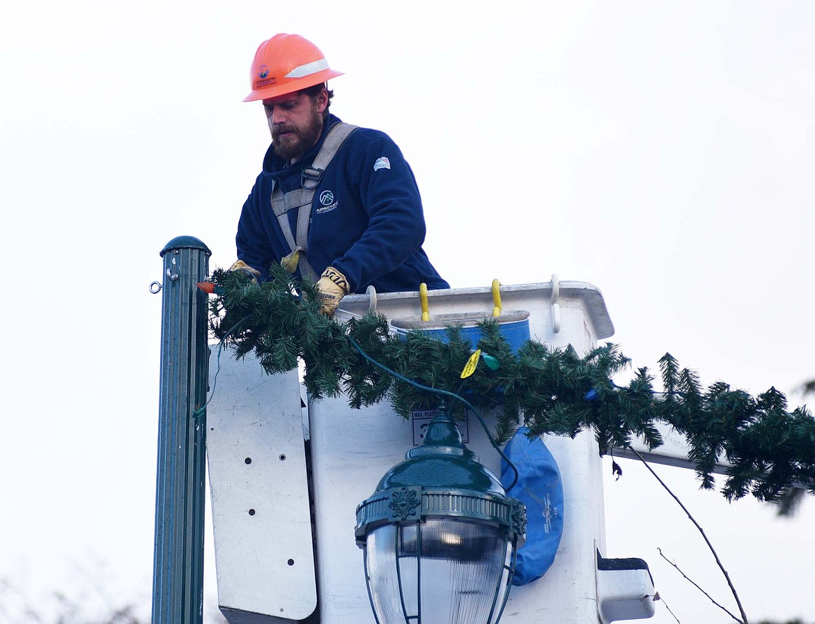 A lineman from Flathead Electric Co-op attaches garland to a light pole downtown Sunday morning. (Heidi Desch/Whitefish Pilot)