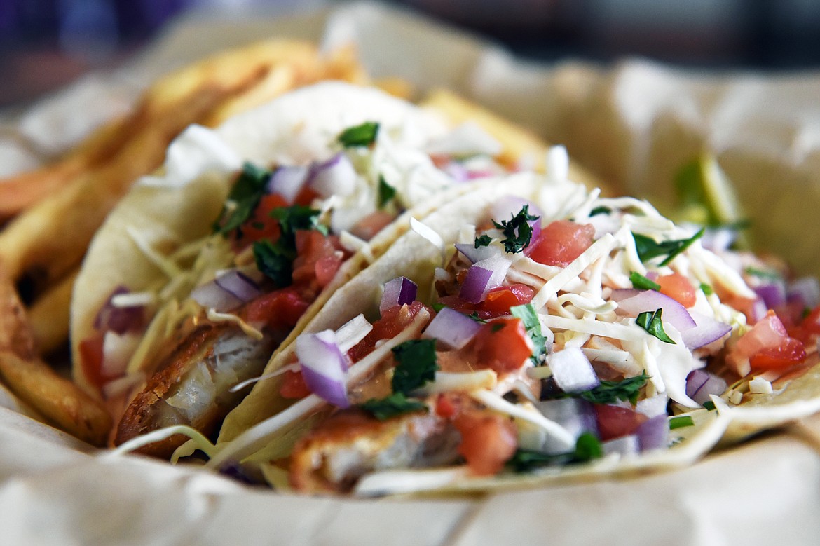 Fish tacos are served in flour tortillas with choice of grilled sockeye salmon or beer-battered cod, garnished with cabbage, tomato, red onion, cilantro and creamy baja sauce with french fries at Fork in the River.