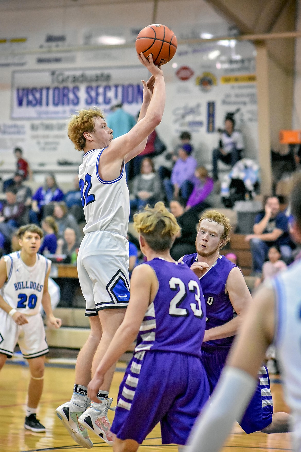 Mission Bulldog junior forward Layne Spidel (32) elevates for a jumper while Charlo Vikings Roper Edwards (23) and Levi Gaustad (33) defend. (Photo courtesy of Christa Umphrey, Forward Photography)