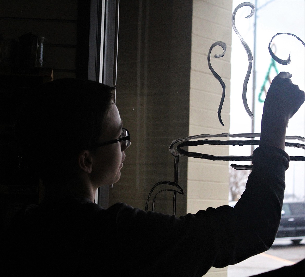 Chris Jones painting a steaming cup of coffee on the front window of the Plains Bistro. (John Dowd/Clark Fork Valley Press)