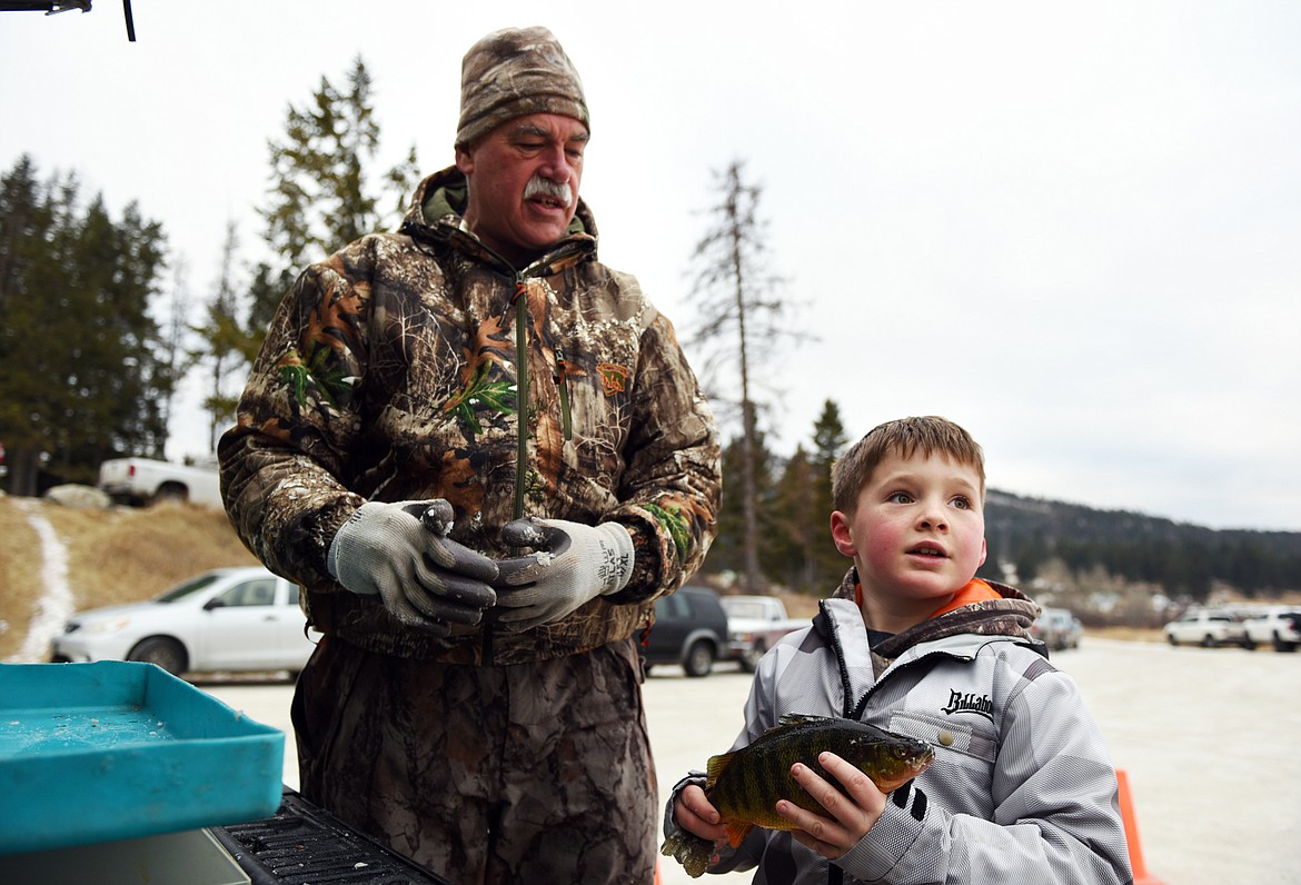 Kwintyn Hicks, of Kalispell, holds a perch to be weighed by Joe Rudolph, left, president of the Flathead Chapter of Walleyes Unlimited at the 49th annual Sunriser Lions ice fishing derby at Smith Lake on Saturday. (Casey Kreider/Daily Inter Lake)