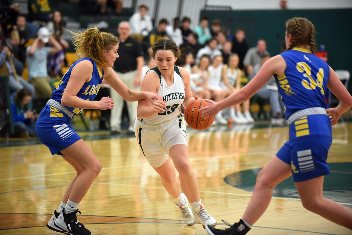 Bulldog Gracie Smyley drives between two Libby defenders Friday night at the Whitefish High School gym. (Heidi Desch/Whitefish Pilot)