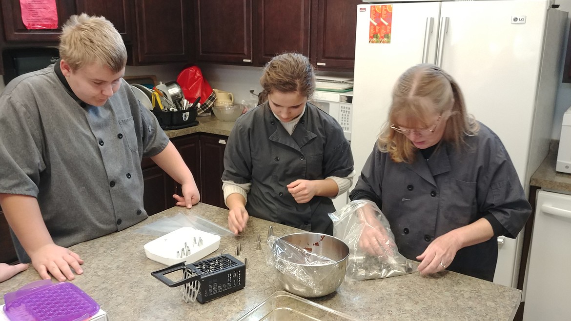 Hot Springs High School culinary arts instructor Brenda Haase works with students Morgan Hoff and Johua Grahan on a cupcake decorating project. (Chuck Bandel/Valley Press)