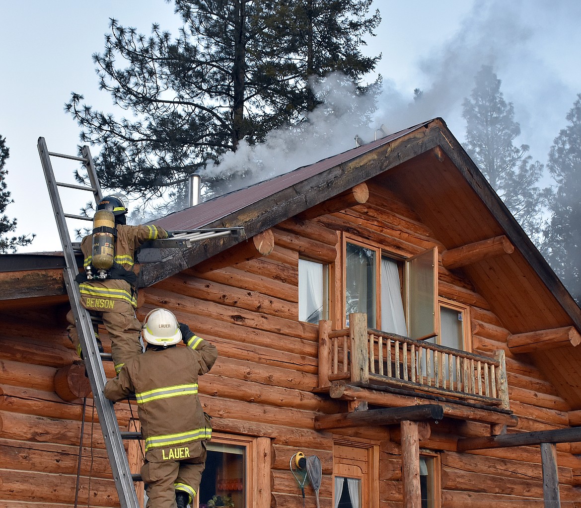 Neil Benson and Steve Lauer of the Libby Volunteer Fire Department battle a fire smoldering beneath the ridge cap of a home near Farm To Market Road on Feb. 21. (Duncan Adams/The Western News)