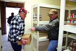 Doug Sharkey directs Ken Christofferson as to where he should set down his box of food.